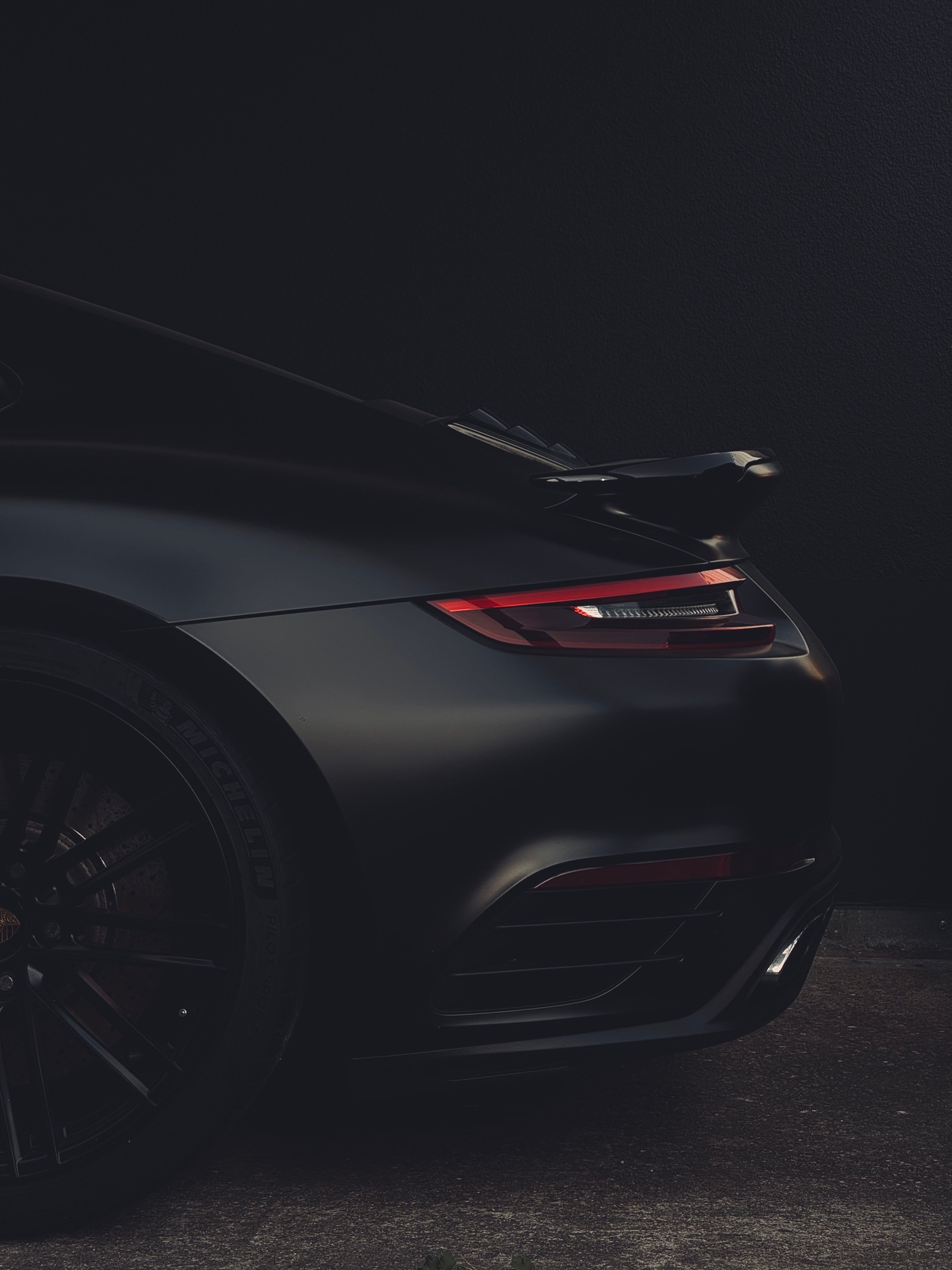 Rear of a matte black Porsche 911 with its tail light glowing